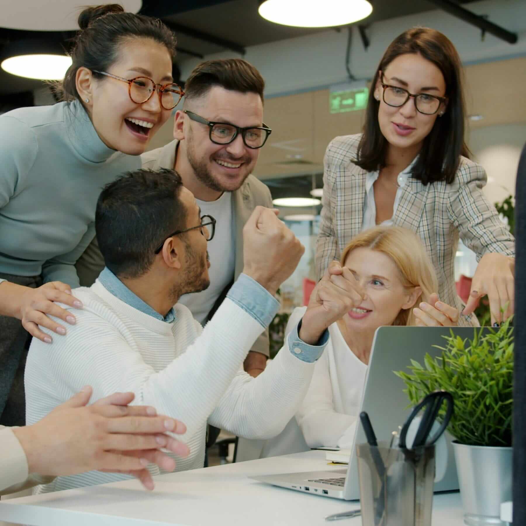 five coworkers happily looking at something exciting on laptop screen